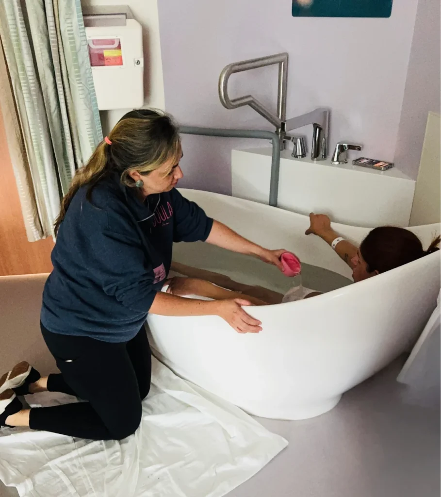 A woman kneeling beside a birth tub, supporting a person in the water