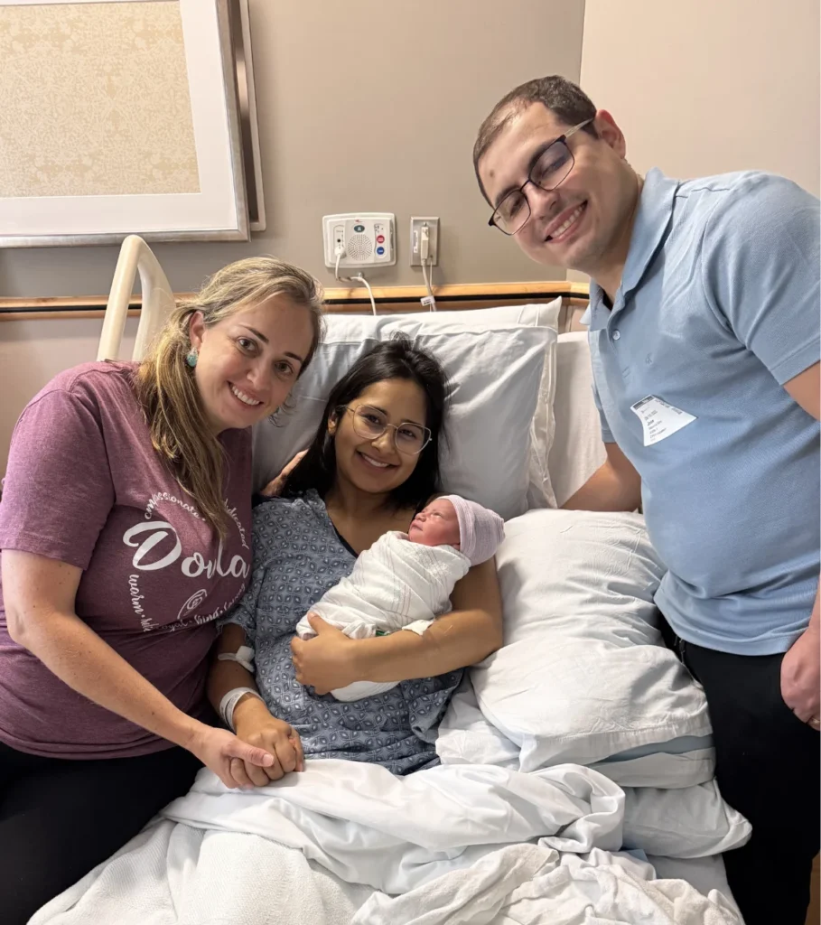 Three smiling adults gathered around a hospital bed with a newborn