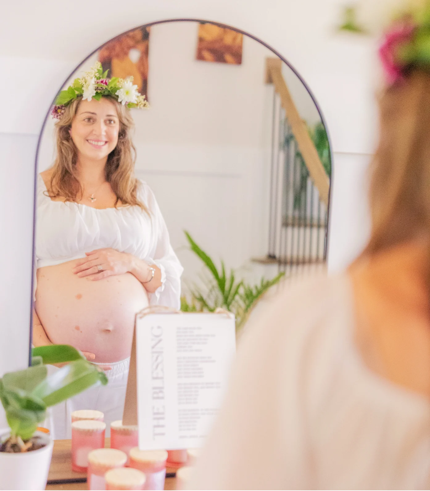 A woman wearing a flower crown looks at her reflection in an arched mirror